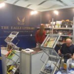 Interior view of The Eagle Literary LLC's exhibition booth at the 2026 Manila International Book Fair, featuring navy blue and gold branding, organized bookshelves, promotional displays, and visitors exploring published literary works.
