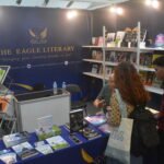 Visitors engaging in a literary discussion with an exhibitor at The Eagle Literary's booth during the 2026 Manila International Book Fair, surrounded by featured books, promotional materials, and author displays.
