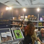 Visitors browsing featured books and interacting with an exhibitor at The Eagle Literary LLC's Booth 2-107 during the 2026 Manila International Book Fair, featuring organized bookshelves, promotional displays, and navy blue and gold branding.