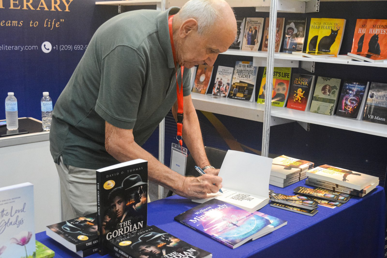 An exhibitor signing a book at The Eagle Literary's booth during the 2026 Manila International Book Fair, surrounded by featured books, promotional materials, and literary displays.