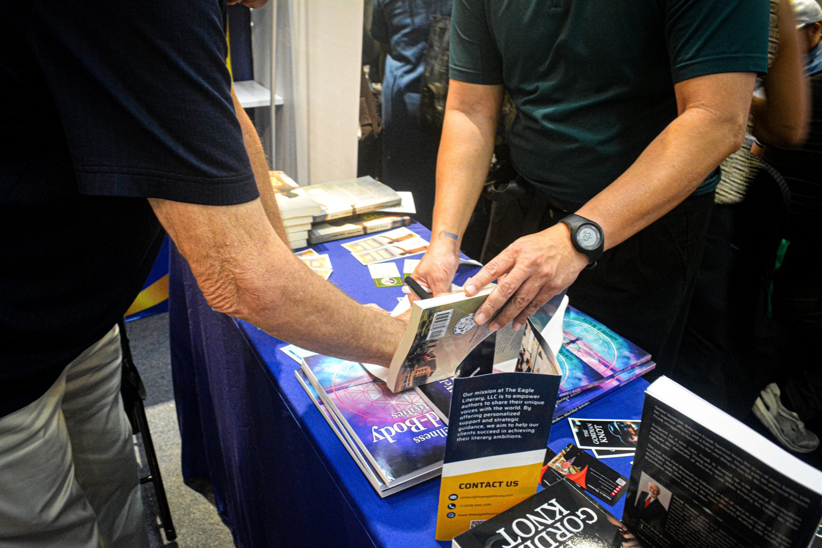 Close-up of two attendees examining a book at The Eagle Literary's booth during the 2026 Manila International Book Fair, featuring displayed books, promotional materials, and literary publications.