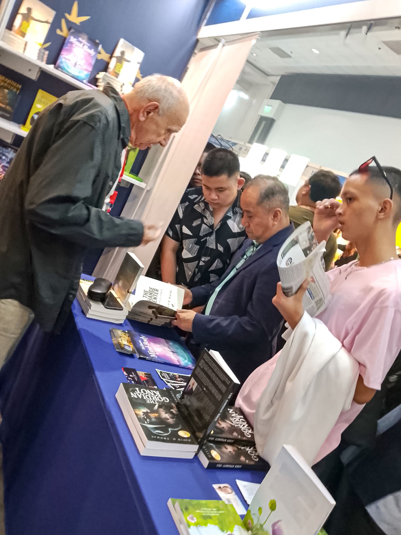 Visitors browsing and examining featured books at The Eagle Literary's exhibition booth during the 2026 Manila International Book Fair, while an exhibitor assists with book selections and literary discussions.