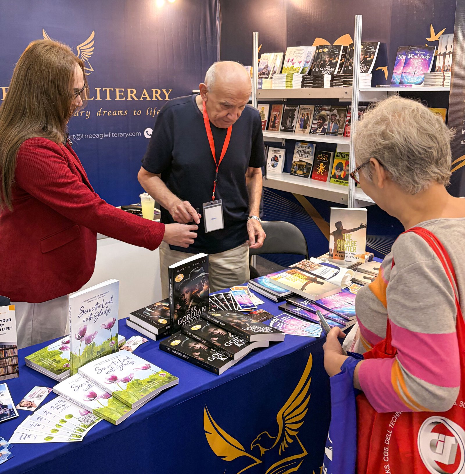 Three attendees engaging in a discussion at The Eagle Literary's exhibition booth during the 2026 Manila International Book Fair, surrounded by featured books, promotional materials, and literary displays.