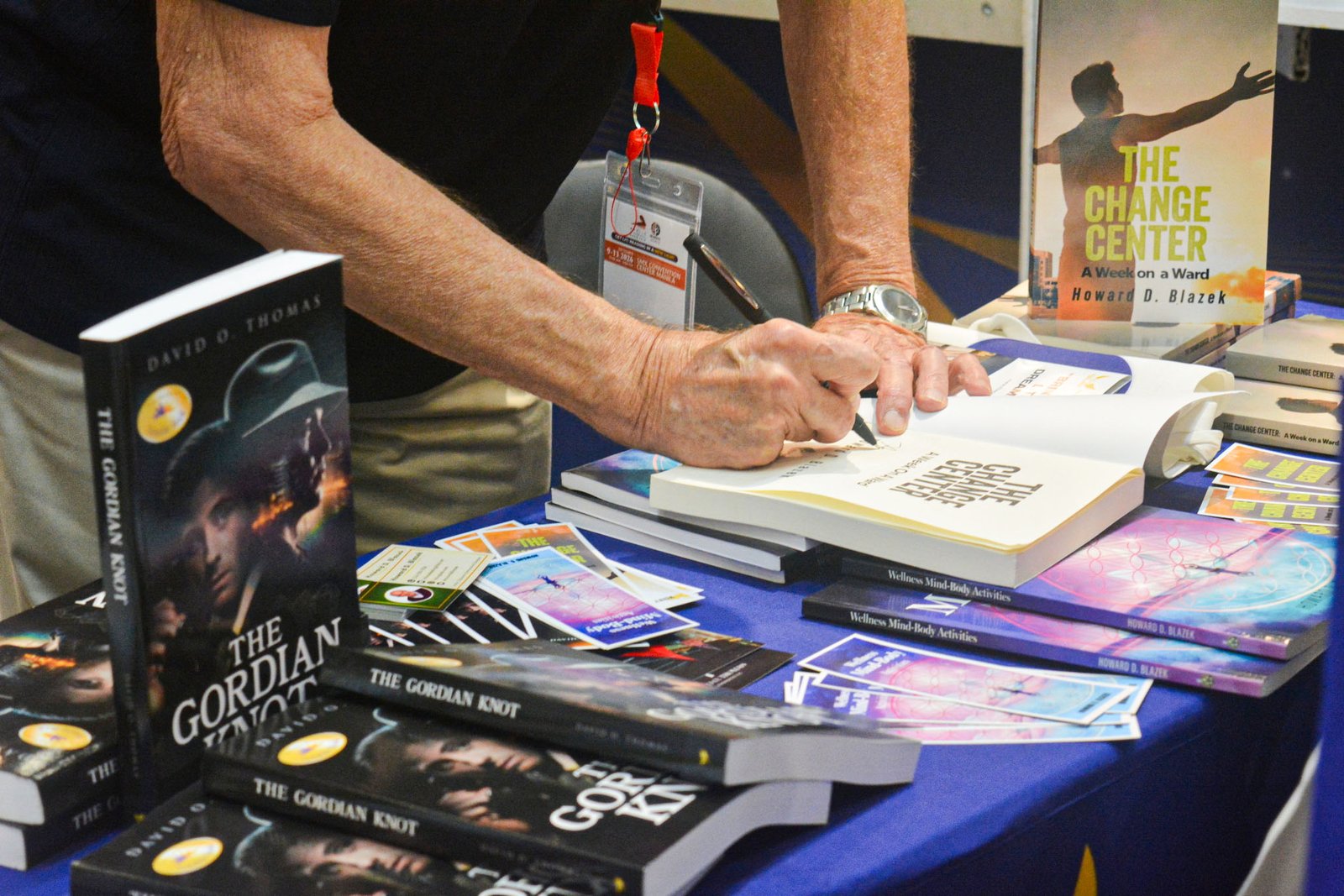 Close-up of an exhibitor signing a copy of The Change Center by Howard D. Blazek at The Eagle Literary's booth during the 2026 Manila International Book Fair, surrounded by featured books and promotional materials.