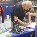 An exhibitor signing a book for a visitor at The Eagle Literary's booth during the 2026 Manila International Book Fair, surrounded by featured publications, promotional materials, and literary displays.